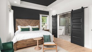 A modern bedroom with a large bed, a small round table, and a chair. There is a sliding door leading to a bathroom. - Huge Rooftop Patio at this Stunning Spacious House (Nashville)