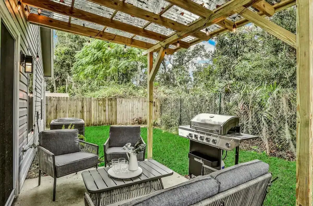 Un patio al aire libre con una parrilla, dos sillas, una mesa y una estructura de pérgola.