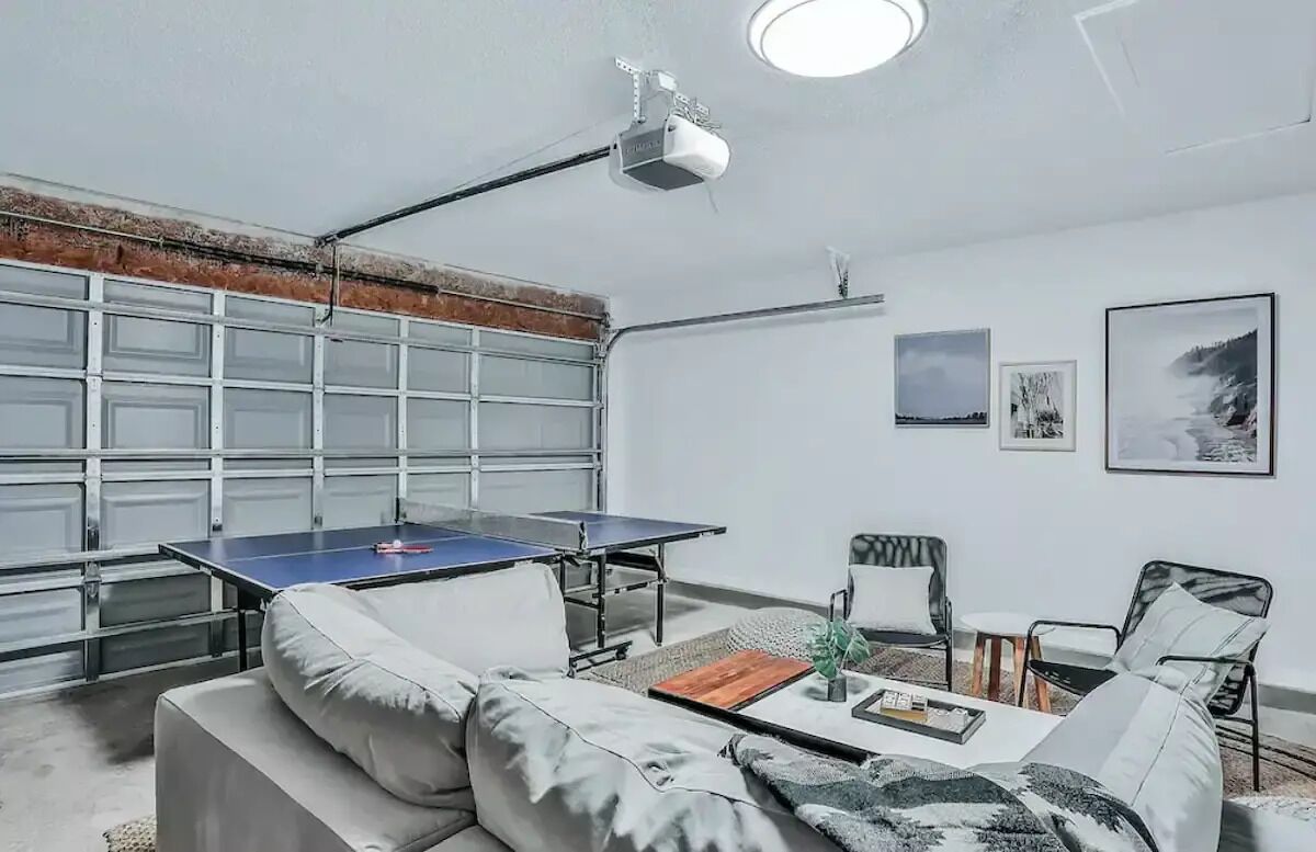 Une pièce équipée d’une table de ping-pong, d’un canapé, d’une table basse et d’un projecteur fixé au plafond.