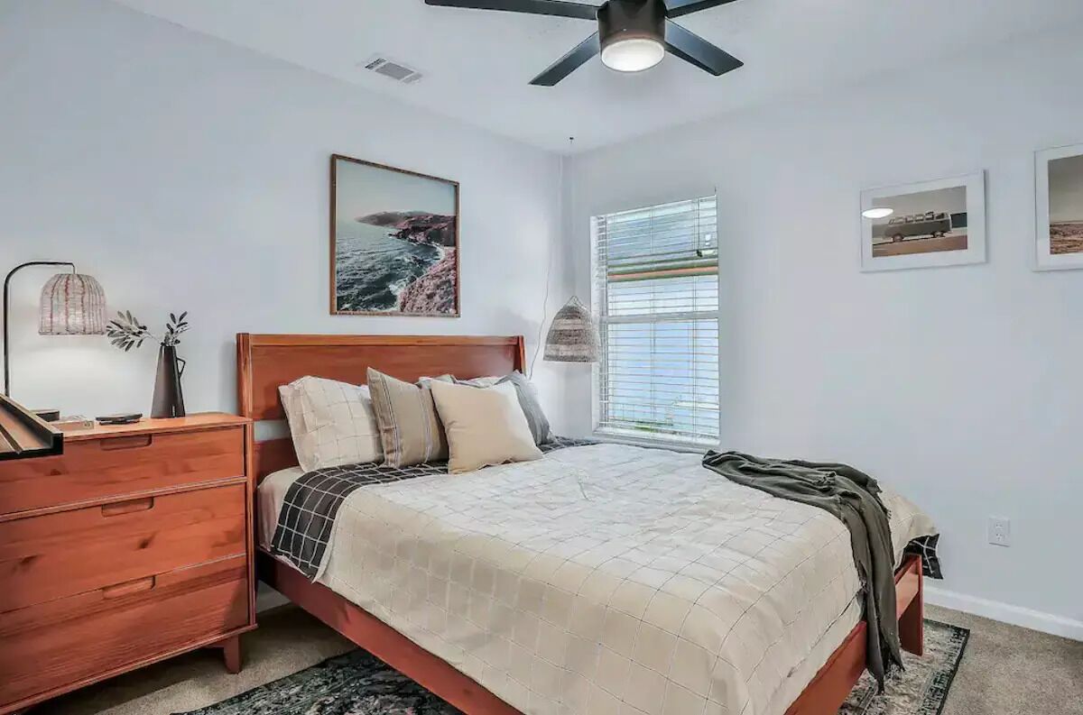 Un dormitorio con cama, mesita de noche, cómoda, ventilador de techo y ventana con persianas.