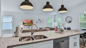 A modern kitchen with a granite countertop, stainless steel sink, and three pendant lights. - Peaceful Escape in Atlantic Beach (Atlantic Beach)