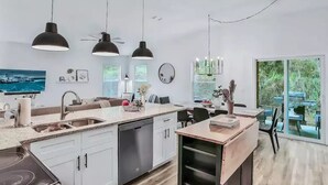 A modern kitchen with white cabinetry, a central island, pendant lighting, and a view of the outdoors through large sliding glass doors. - Peaceful Escape in Atlantic Beach (Atlantic Beach)