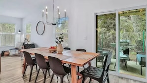 A dining area with a wooden table, black chairs, a chandelier, and a large window with a view of greenery. - Peaceful Escape in Atlantic Beach (Atlantic Beach)