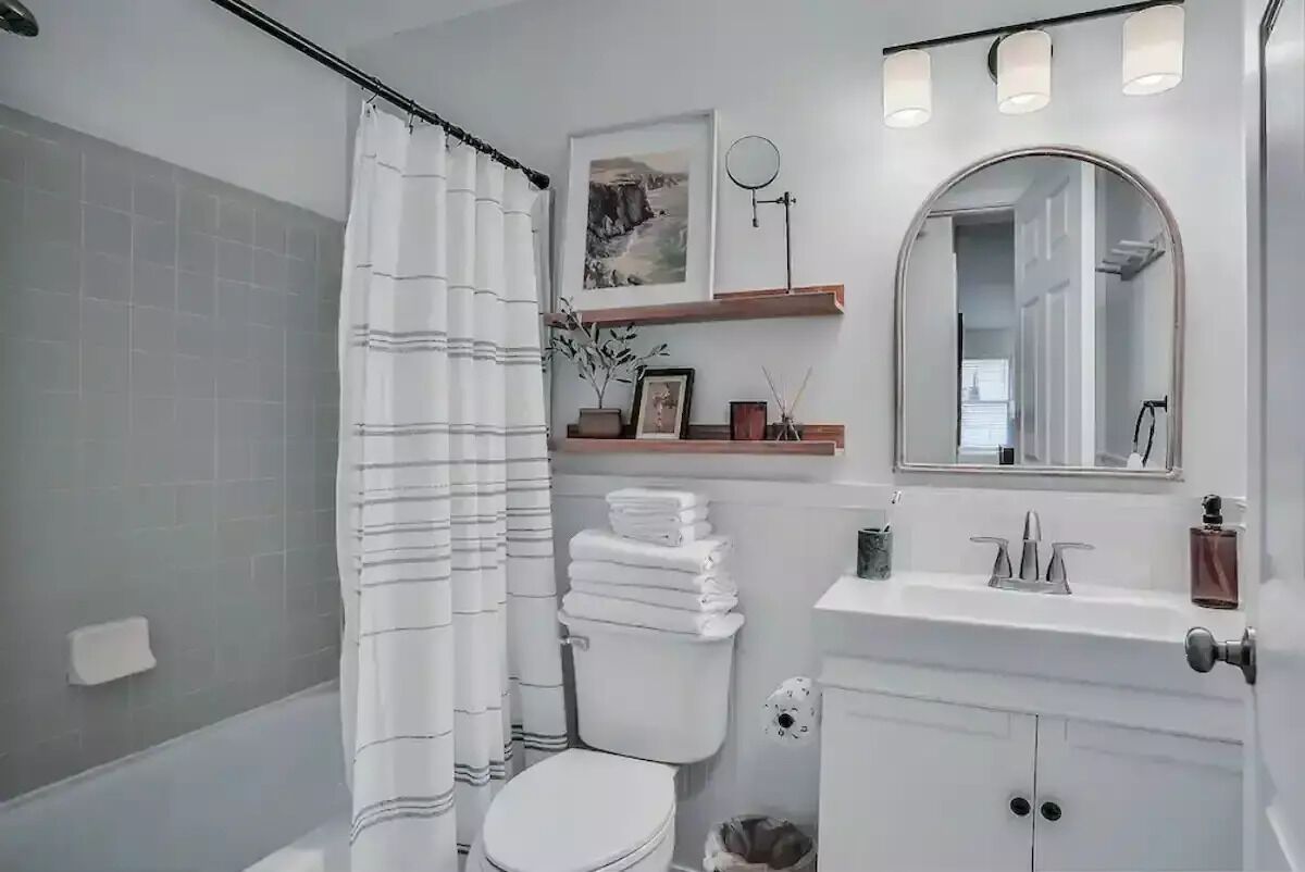 Ein Badezimmer mit Toilette, Duschvorhang, Waschbecken mit Spiegel und Ablage für Toilettenartikel.