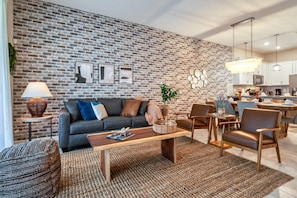 Una sala de estar moderna con pared de ladrillo, un sofá, una mesa de centro y un comedor con sillas y una mesa.