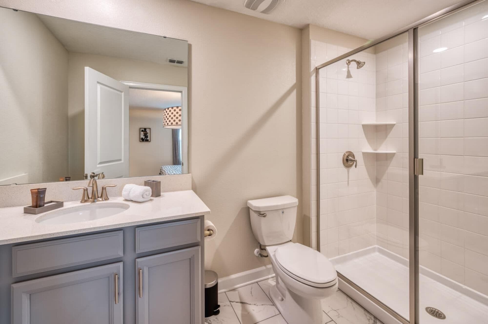 A modern bathroom with a large mirror, a sink with a vanity, a toilet, and a glass-enclosed shower area.