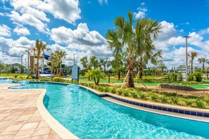 Relax by the pool surrounded by lush greenery and palm trees, with a water slide and lifeguard tower for a safe and fun experience.