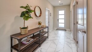 A hallway with a wooden console table, a potted plant, a mirror, and a door with a frosted glass panel. - Chic Luxury Decor Prime Location Game Room Bliss (Kissimmee)