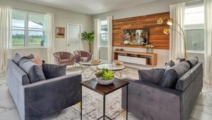 A modern living room with a grey sofa set, a coffee table with a bowl of fruit, and a TV mounted on a wooden wall. - Chic Luxury Decor Prime Location Game Room Bliss (Kissimmee)