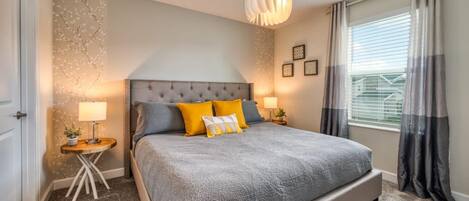Un dormitorio con una cama grande, dos mesitas de noche, una lámpara colgante, una ventana con cortinas y un papel tapiz con estampado floral.