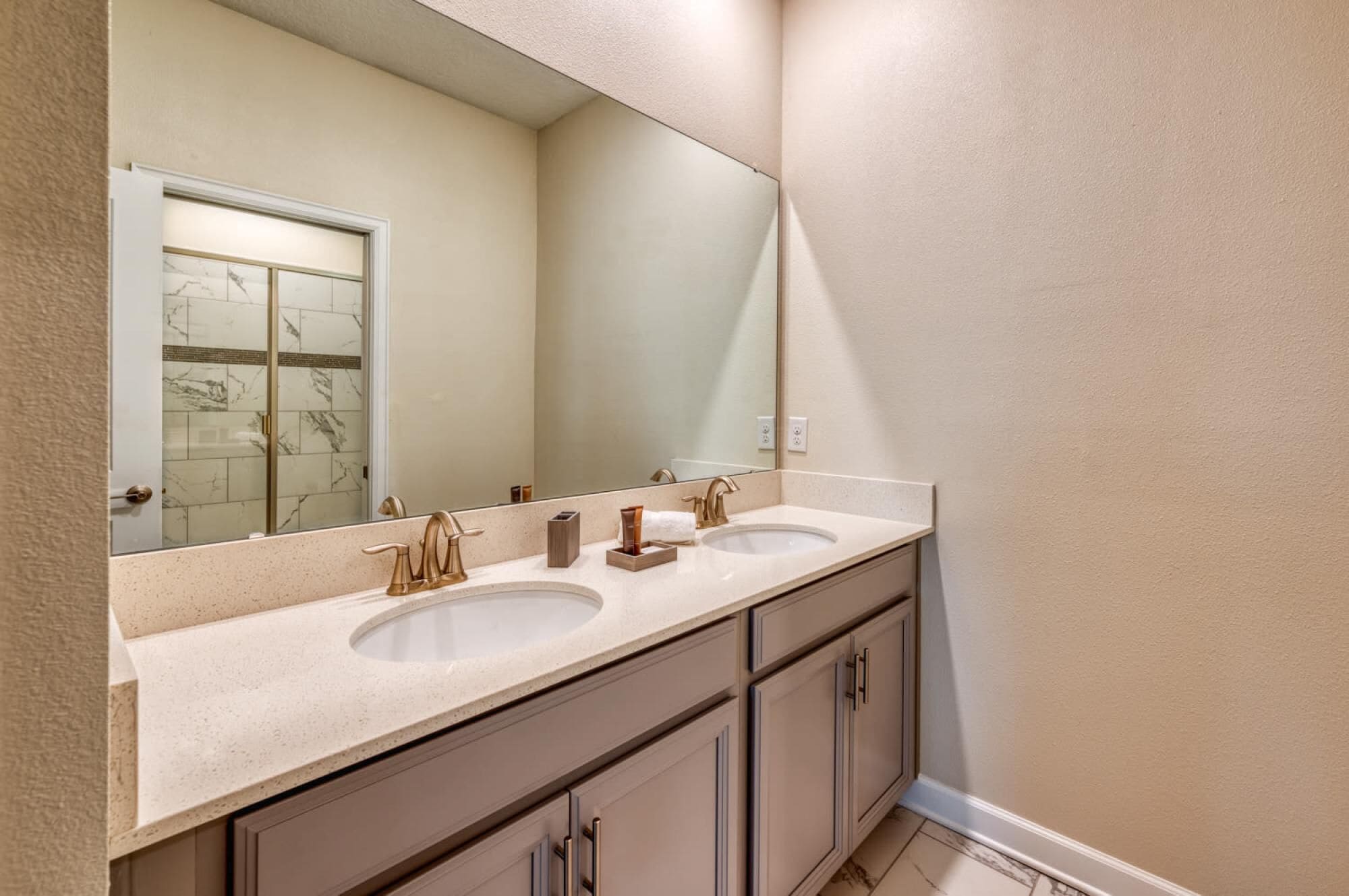 Une salle de bain avec deux lavabos, un grand miroir et une douche aux carreaux de marbre.