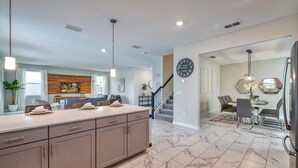 A modern kitchen with a marble floor, a dining area with a chandelier, and a staircase leading to another level. - Chic Luxury Decor Prime Location Game Room Bliss (Kissimmee)
