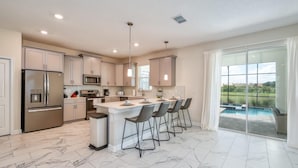 A modern kitchen with a large island, stainless steel appliances, and a view of a swimming pool. - Chic Luxury Decor Prime Location Game Room Bliss (Kissimmee)