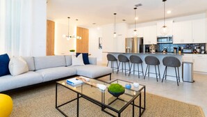 A modern living room with a sofa, coffee table, and bar stools. - Chic Modern Marvel-spacious Themed Bedrooms Private Pool (Kissimmee)