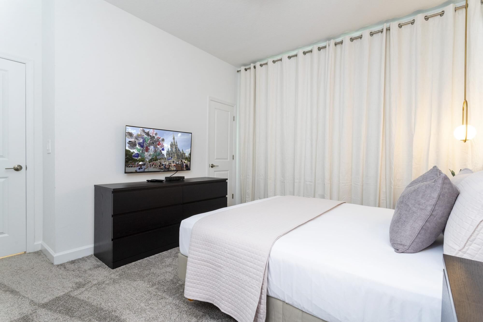 A bedroom with a bed, a TV on a black dresser, and a curtain.