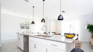 A modern kitchen with white cabinetry, a stainless steel sink, and black pendant lights. - Comfy Themed Home Private Pool Prime Location (Davenport)