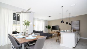 A modern living room with a dining area, a sofa, a TV, and a kitchen island. - Comfy Themed Home Private Pool Prime Location (Davenport)
