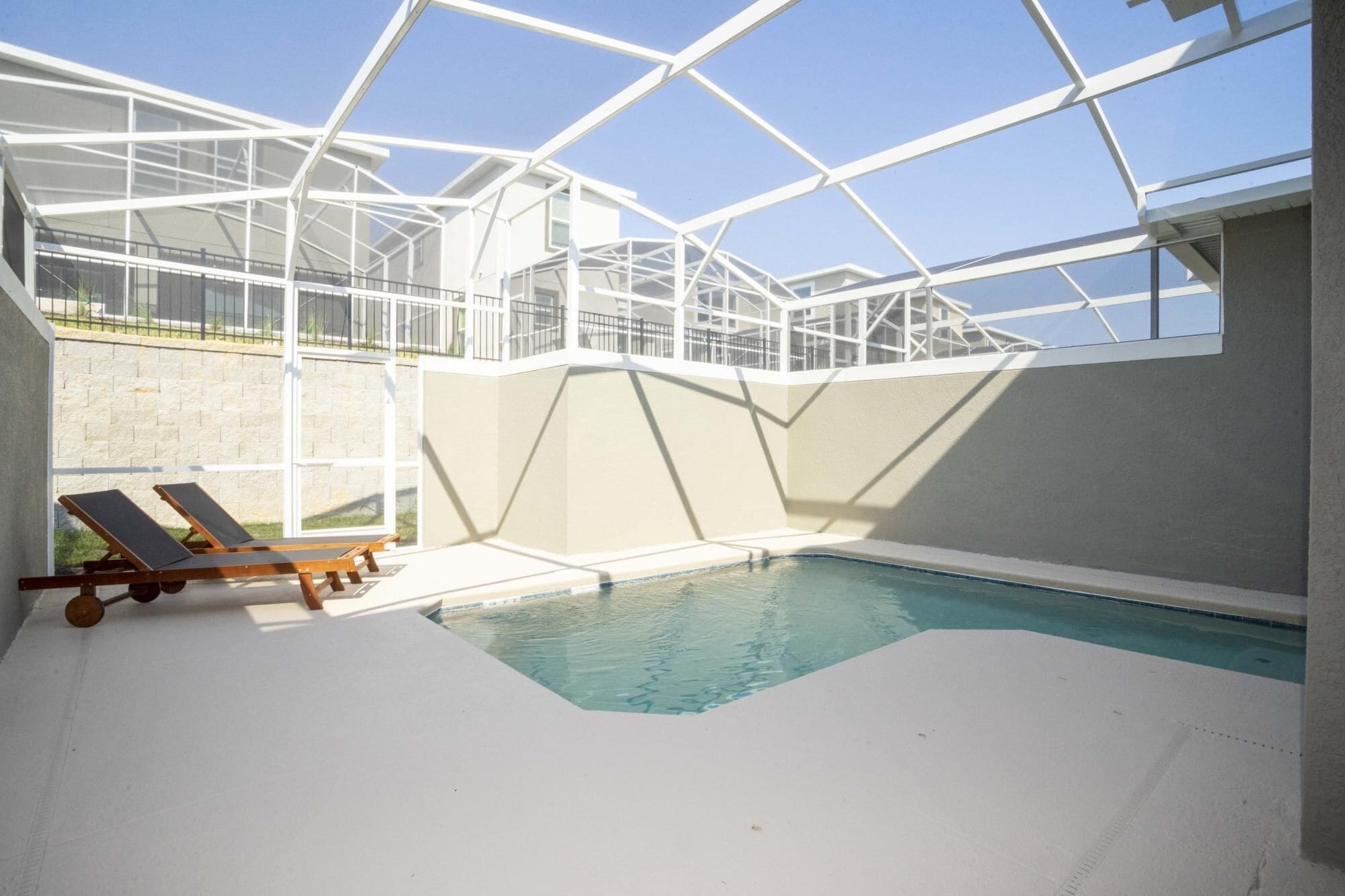 An indoor swimming pool with a glass ceiling, two lounge chairs, and a stone wall in the background.