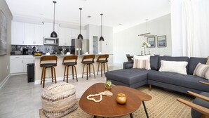 A modern living room with a grey sofa, a coffee table, and a dining area with wooden chairs. - Comfy Themed Home Private Pool Prime Location (Davenport)