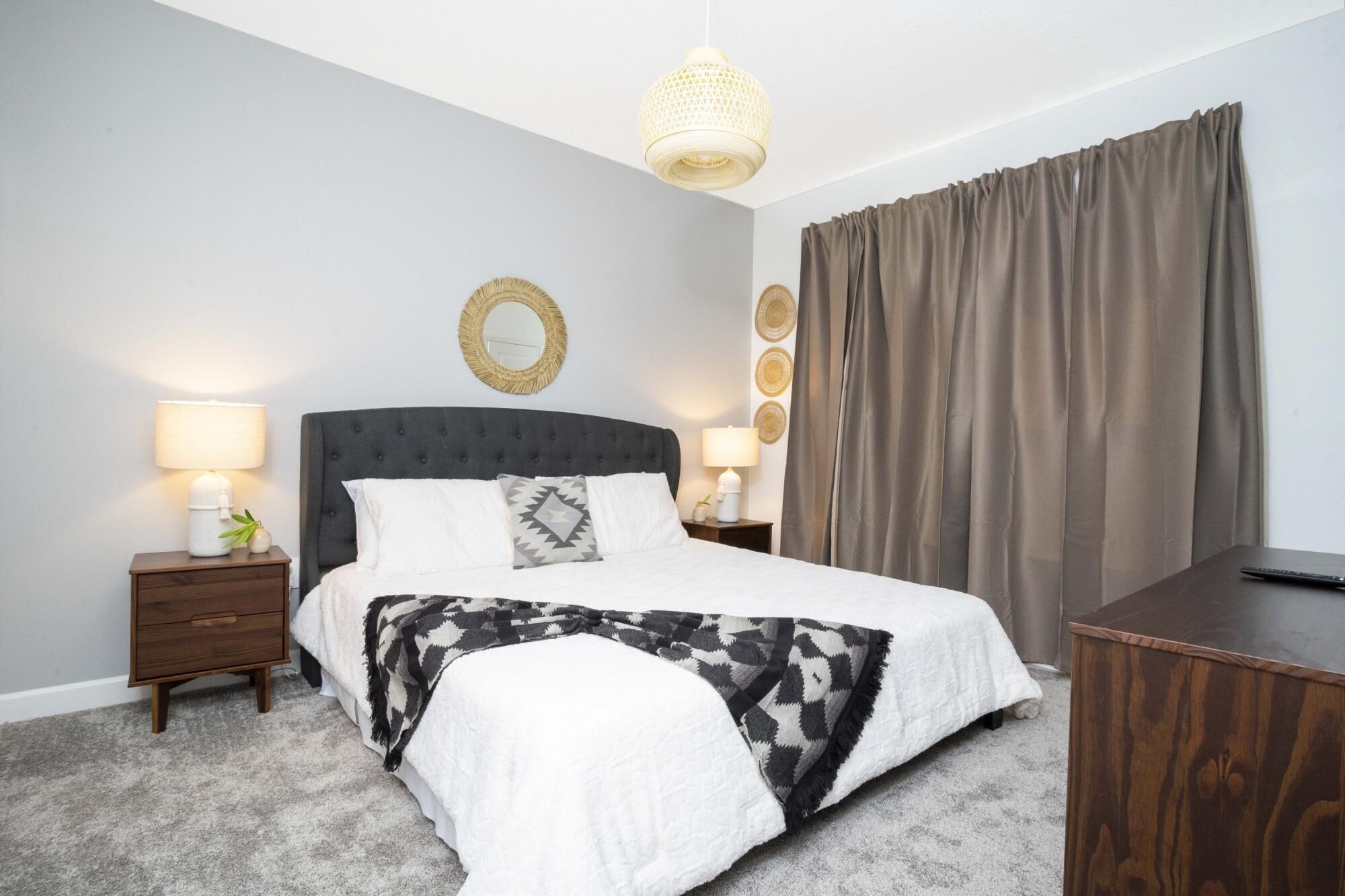 A bedroom with a bed, two bedside tables, a lamp, a mirror, and a desk.