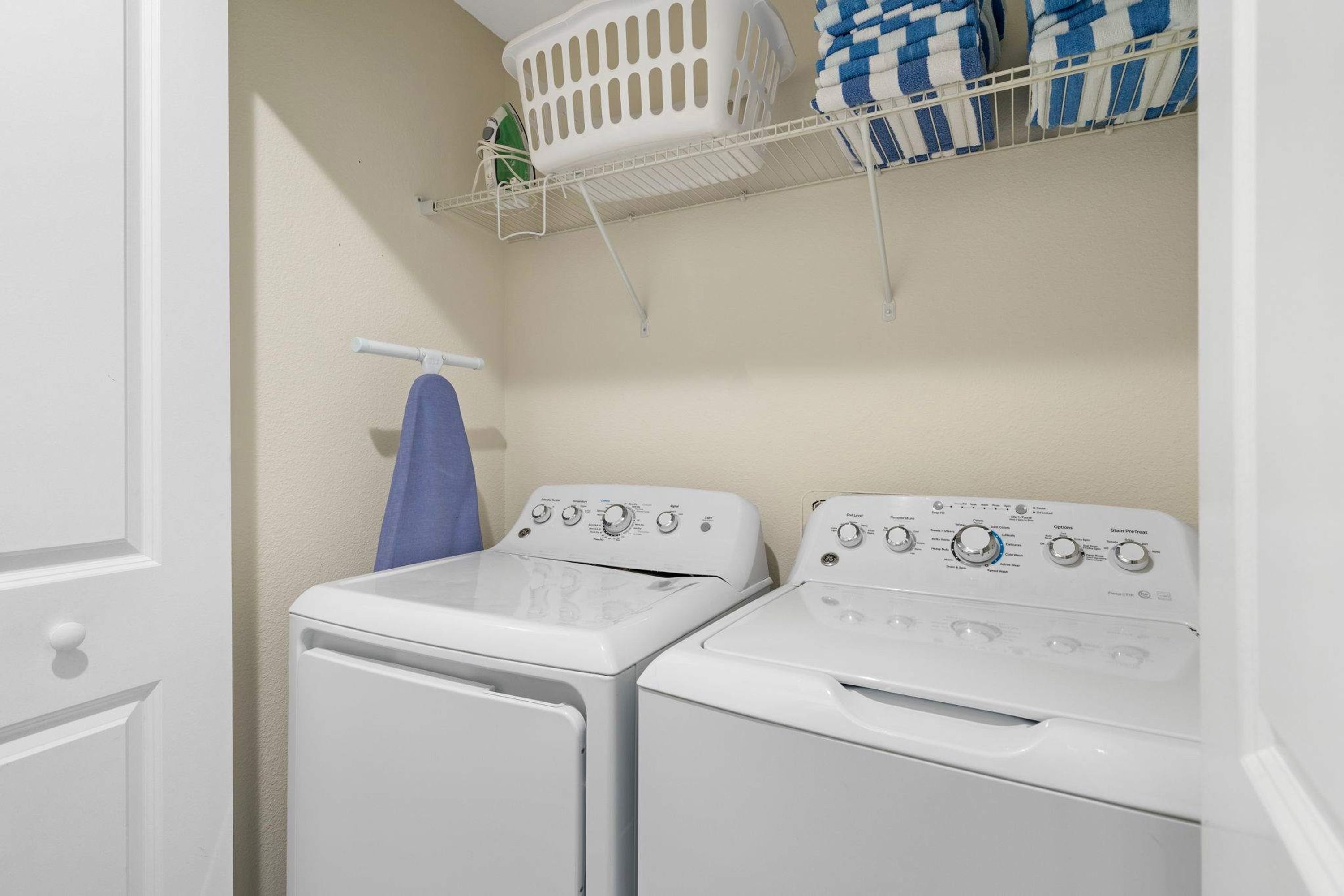 A laundry room with two stacked washers and dryers, a drying rack, and a shelf with folded towels.