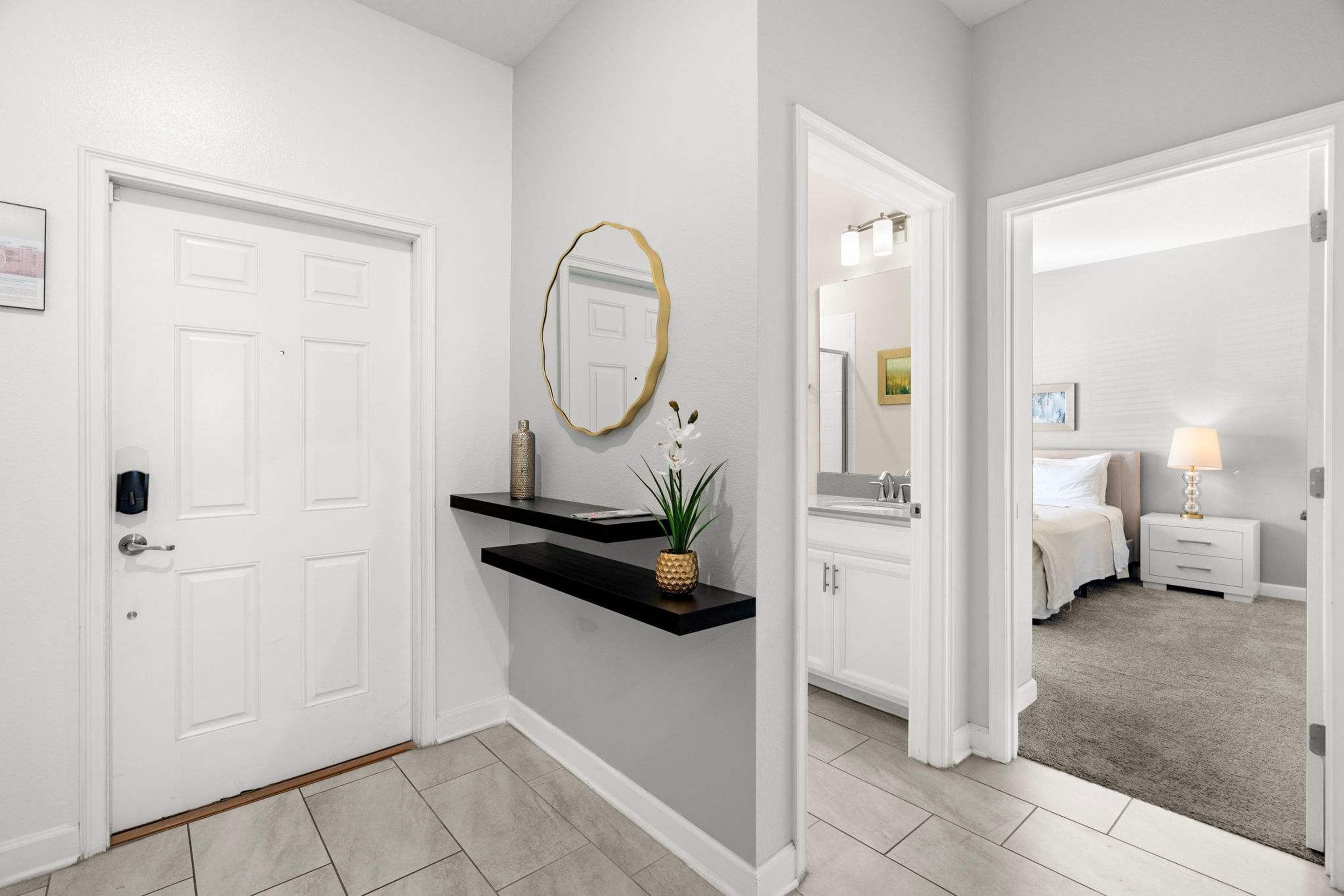 A hallway with a white door, a black floating shelf with a plant, and a mirror on the wall.