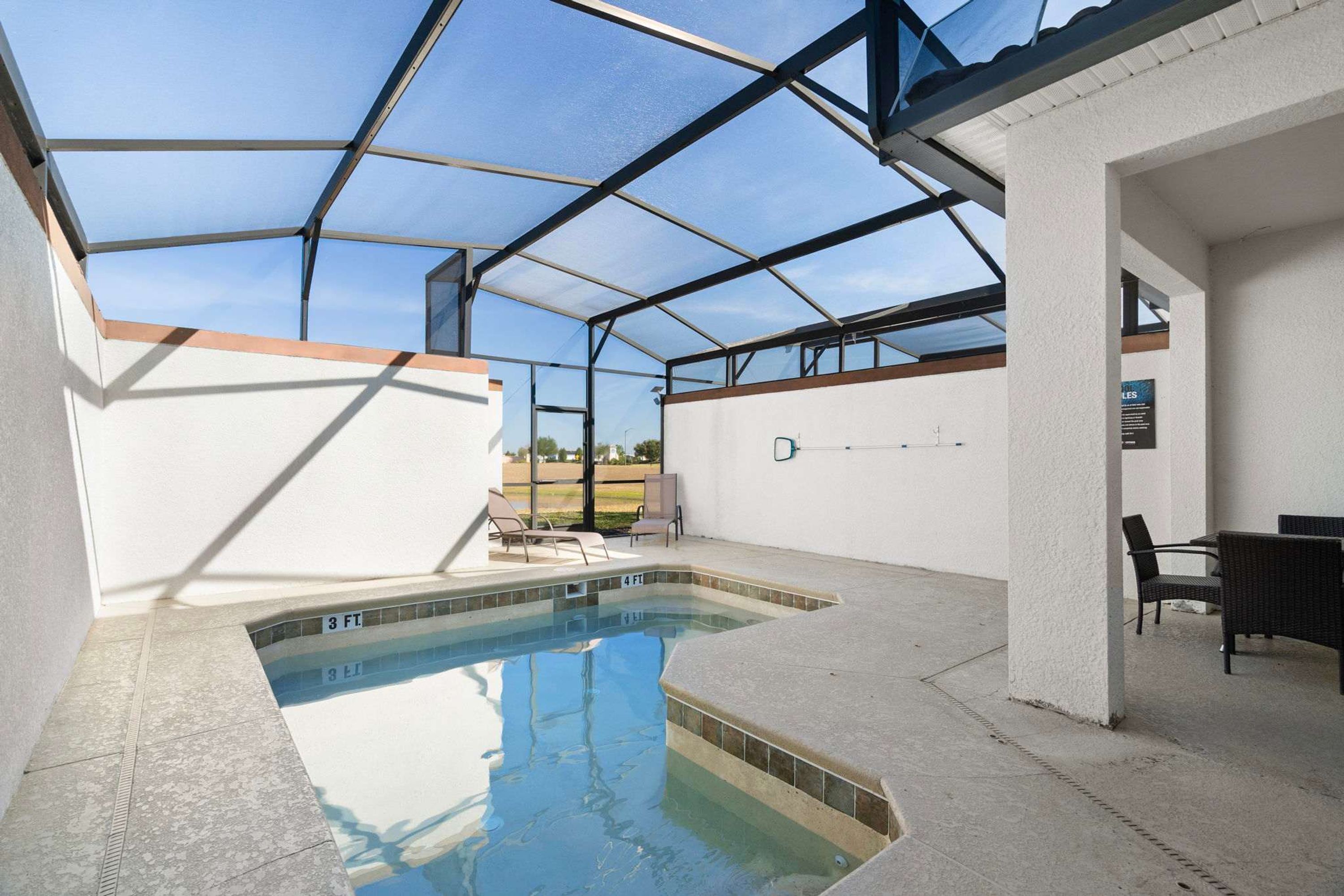 Une piscine intérieure couverte avec un toit en verre, un espace détente avec des fauteuils et une vue sur l’extérieur.
