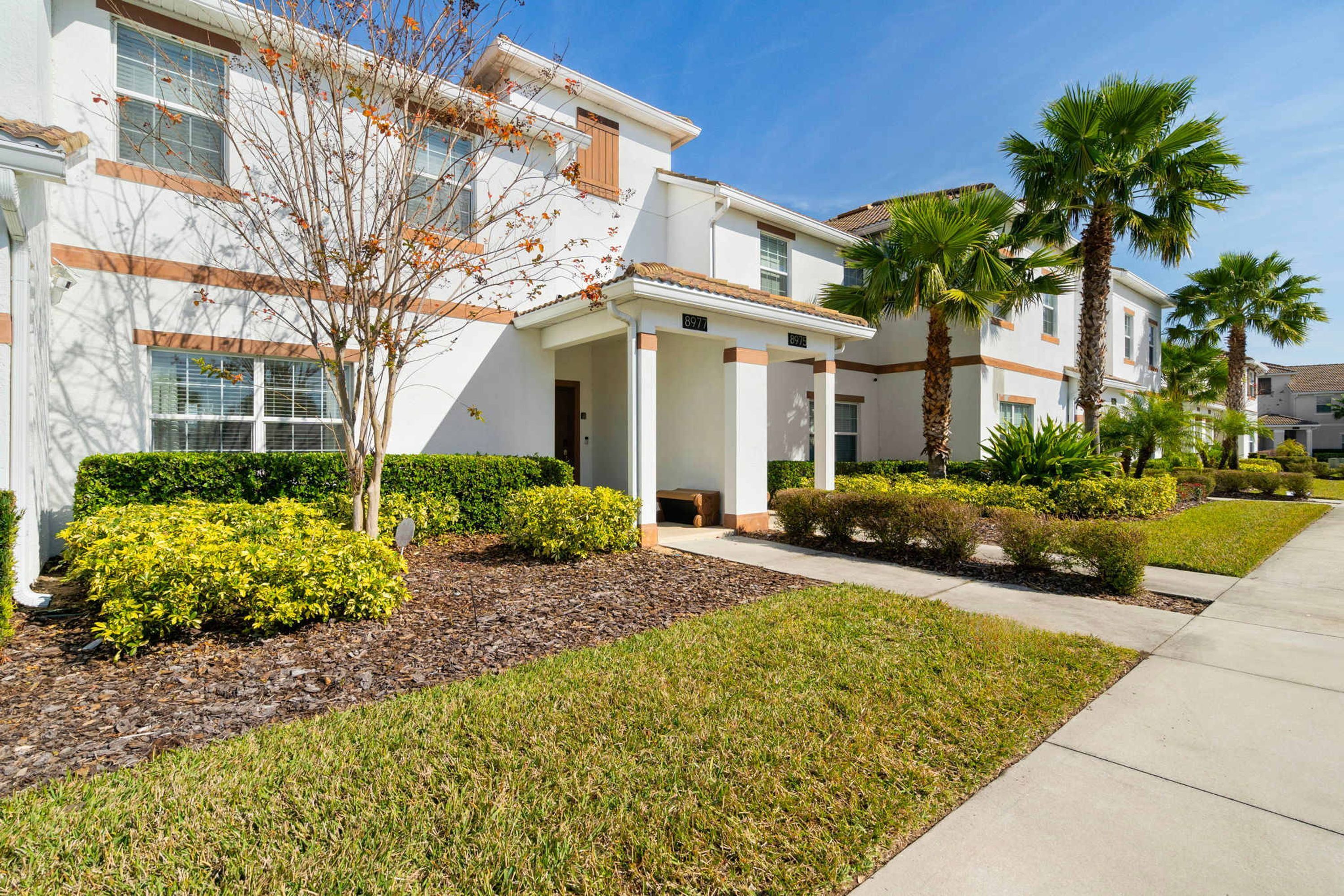 A modern residential building with a well-maintained lawn, palm trees, and a clear sky.
