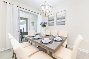 A dining area with a wooden table set for six, white chairs, a chandelier, and framed artwork on the wall.