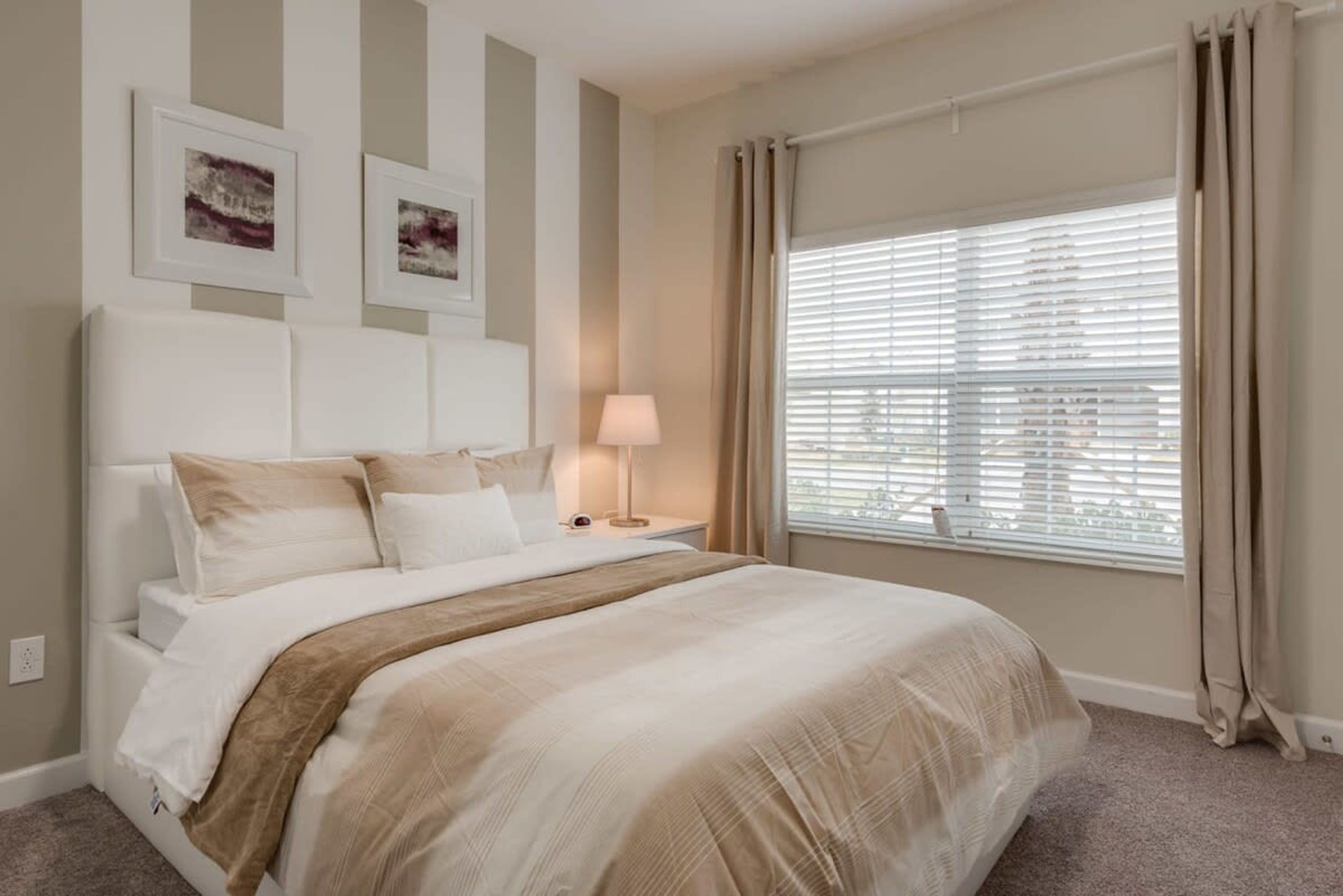A neatly arranged bedroom with a large bed, a bedside table with a lamp, and a window with blinds.