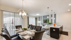 A modern dining area with a large table set for six, surrounded by dark leather chairs. - Cozy Home Prime Disney Parks Location (Kissimmee)