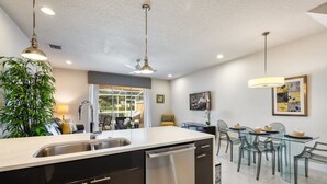 Una cocina moderna con una isla grande, electrodomésticos de acero inoxidable y un comedor con mesa y sillas de vidrio.