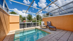 Una piscina exterior techada con techo de vidrio, dos sillones de descanso y vista al vecindario.