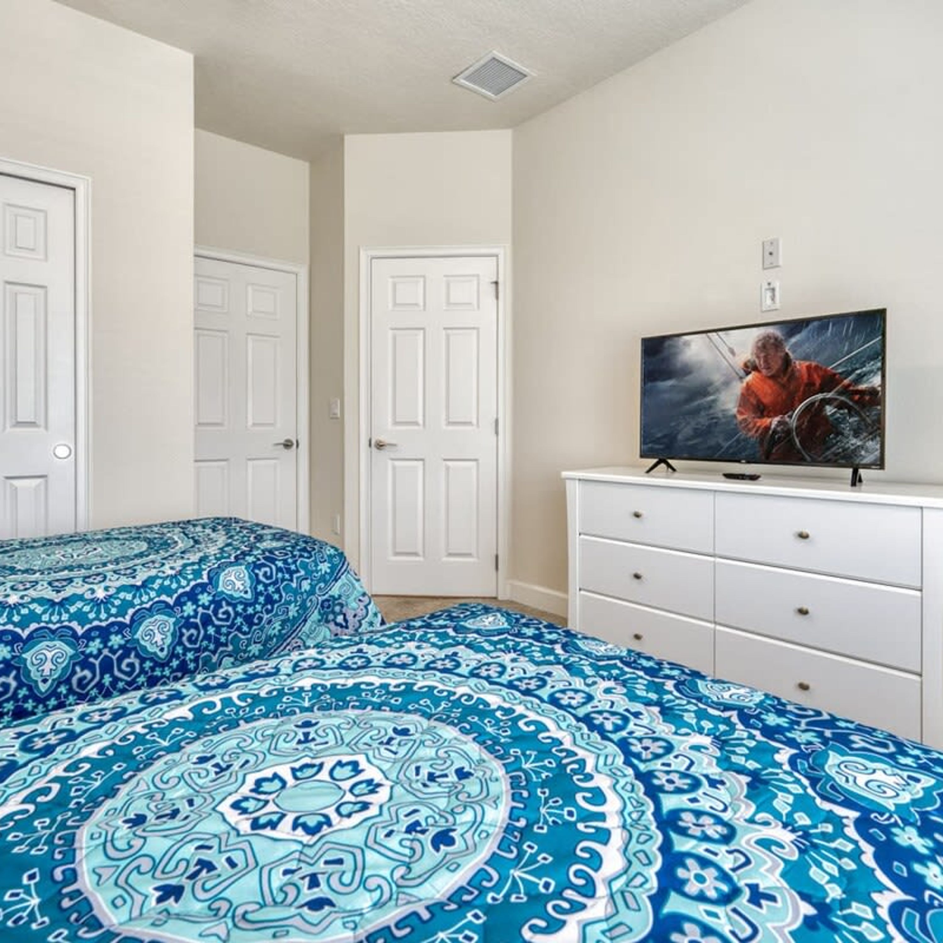 Un dormitorio con dos camas, un televisor sobre un mueble y puertas blancas.