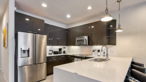 Una cocina moderna con electrodomésticos de acero inoxidable, una isla central e iluminación colgante.
