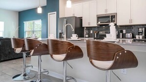 A modern kitchen with white cabinets, stainless steel appliances, and a central island with bar stools. - Cozy Getaways - Spacious Ideal Location (Davenport)