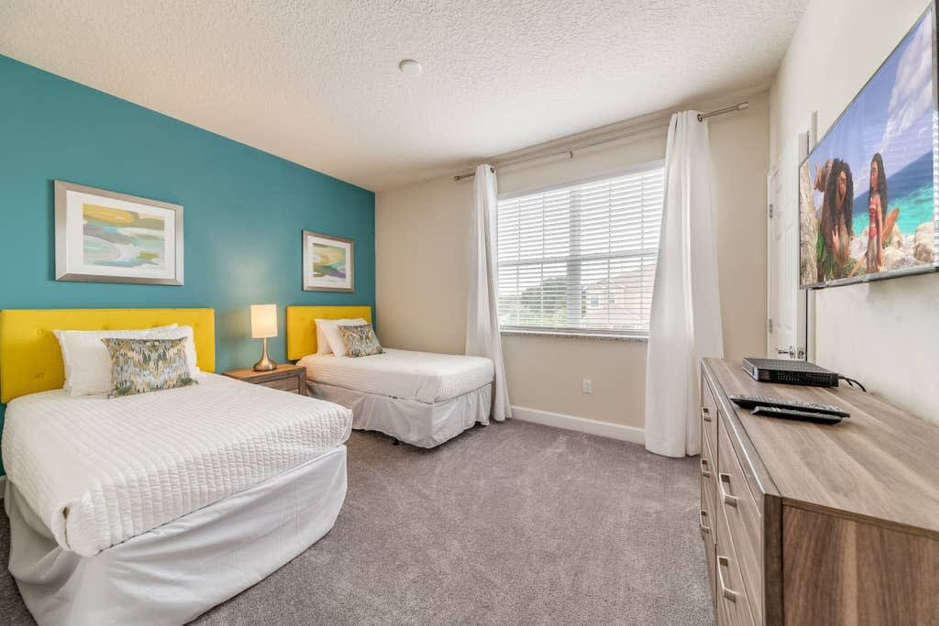 A bedroom with two beds, a desk, and a window with curtains.