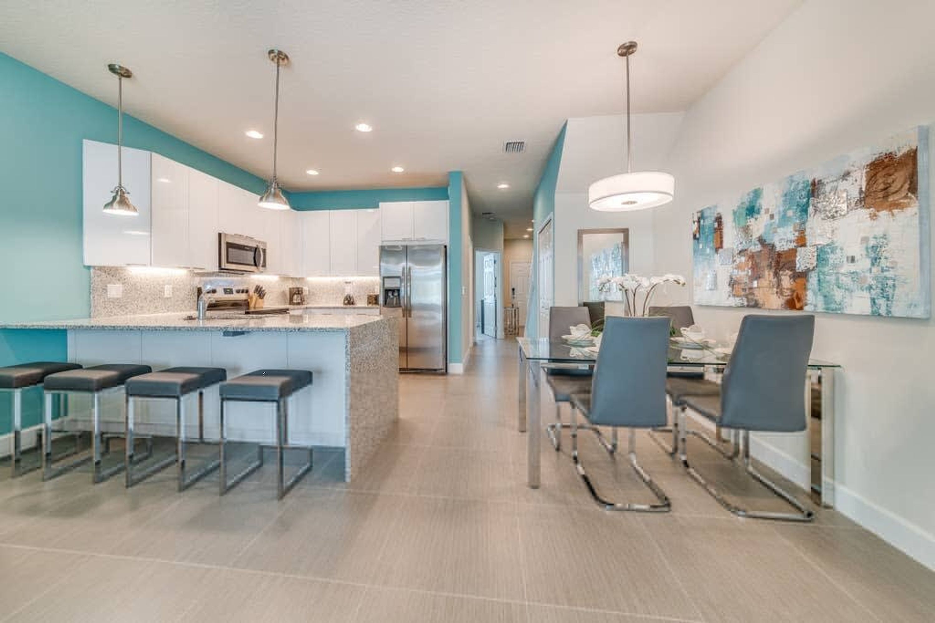 A modern kitchen with a central island, bar stools, and a dining area with chairs.