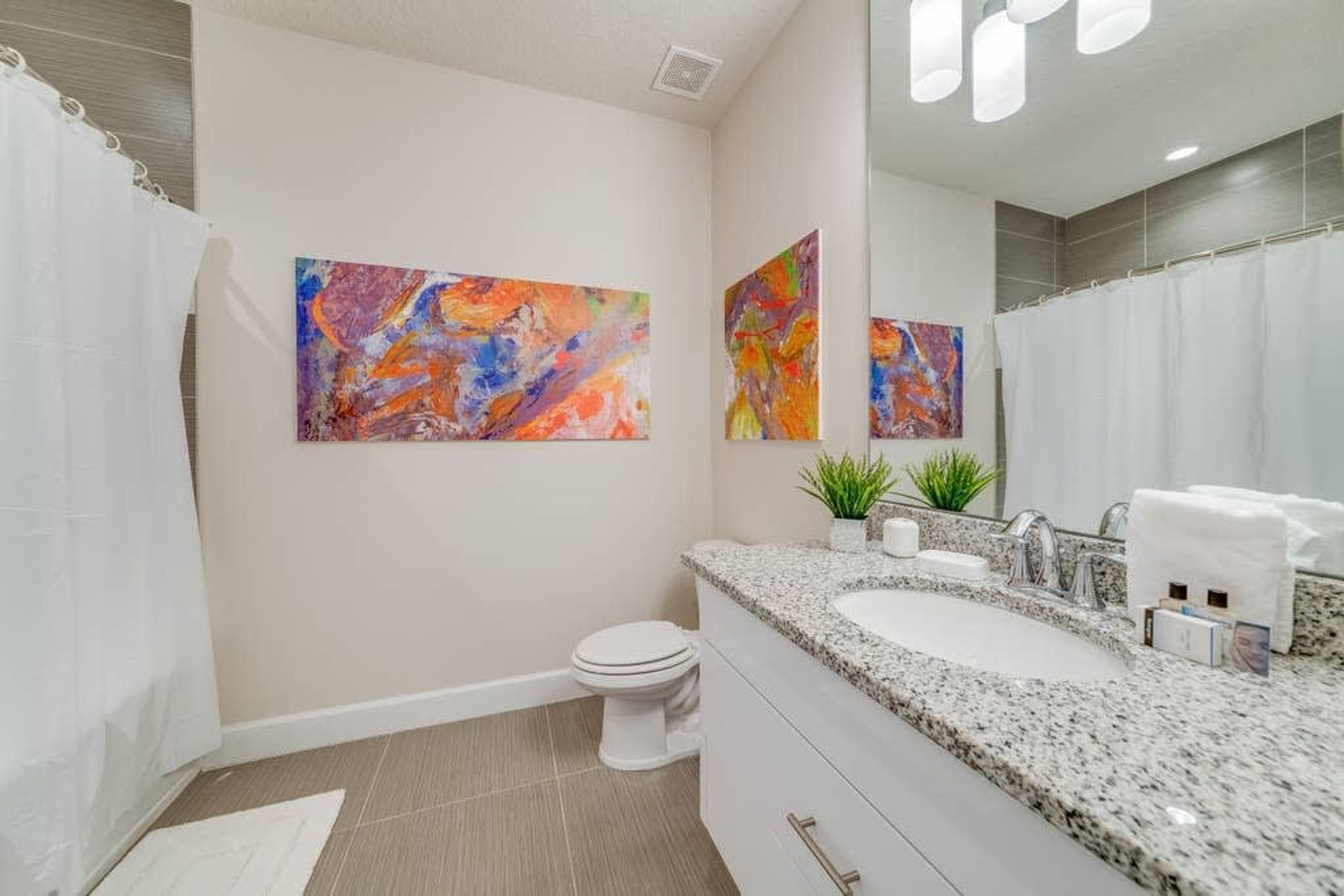 A modern bathroom with a granite countertop, a white toilet, and two abstract paintings on the wall.
