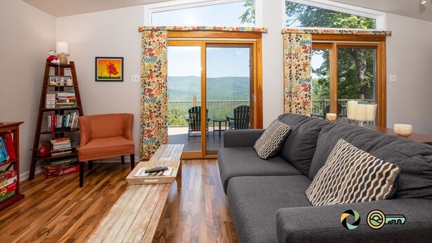 A living room with a sofa, armchair, and bookshelf. There is a sliding glass door leading to an outdoor area with chairs. - Sparkling Bear Lodge | Epic views! | Touch the stars (Mount Jackson)