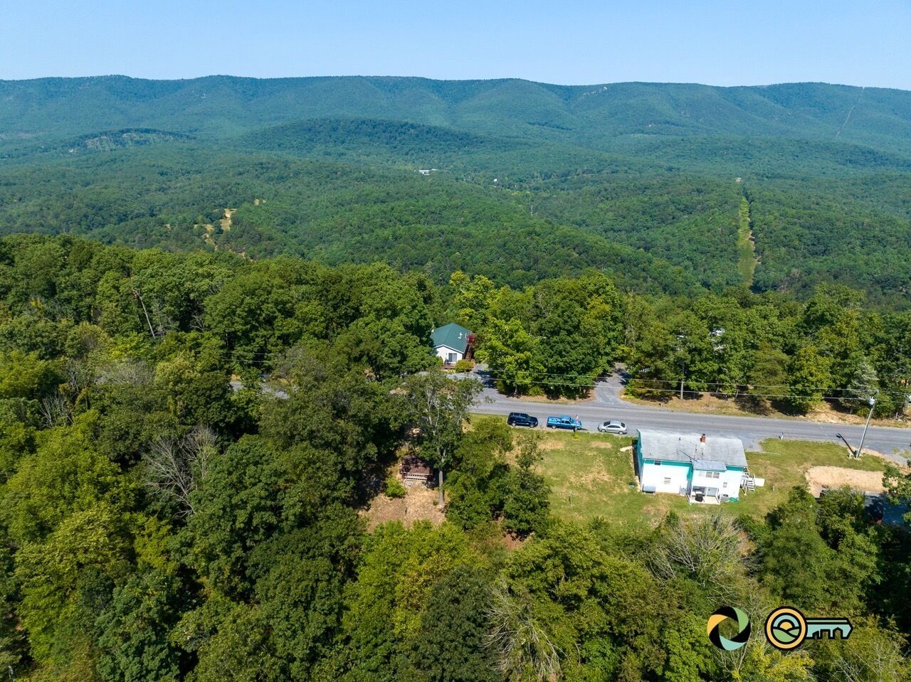 A rural property with a house surrounded by dense forest, a road, and a small clearing.