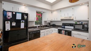 A modern kitchen with white cabinets, a black refrigerator, a wooden countertop, and a view of pink flowers through the window. - Sparkling Bear Lodge | Epic views! | Touch the stars (Mount Jackson)
