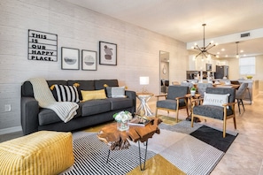 Uma sala de estar moderna com um sofá cinzento, uma mesa de centro e um espaço de jantar com cadeiras.