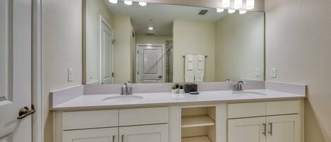 A bathroom with two sinks, a large mirror, and a vanity with cabinets.