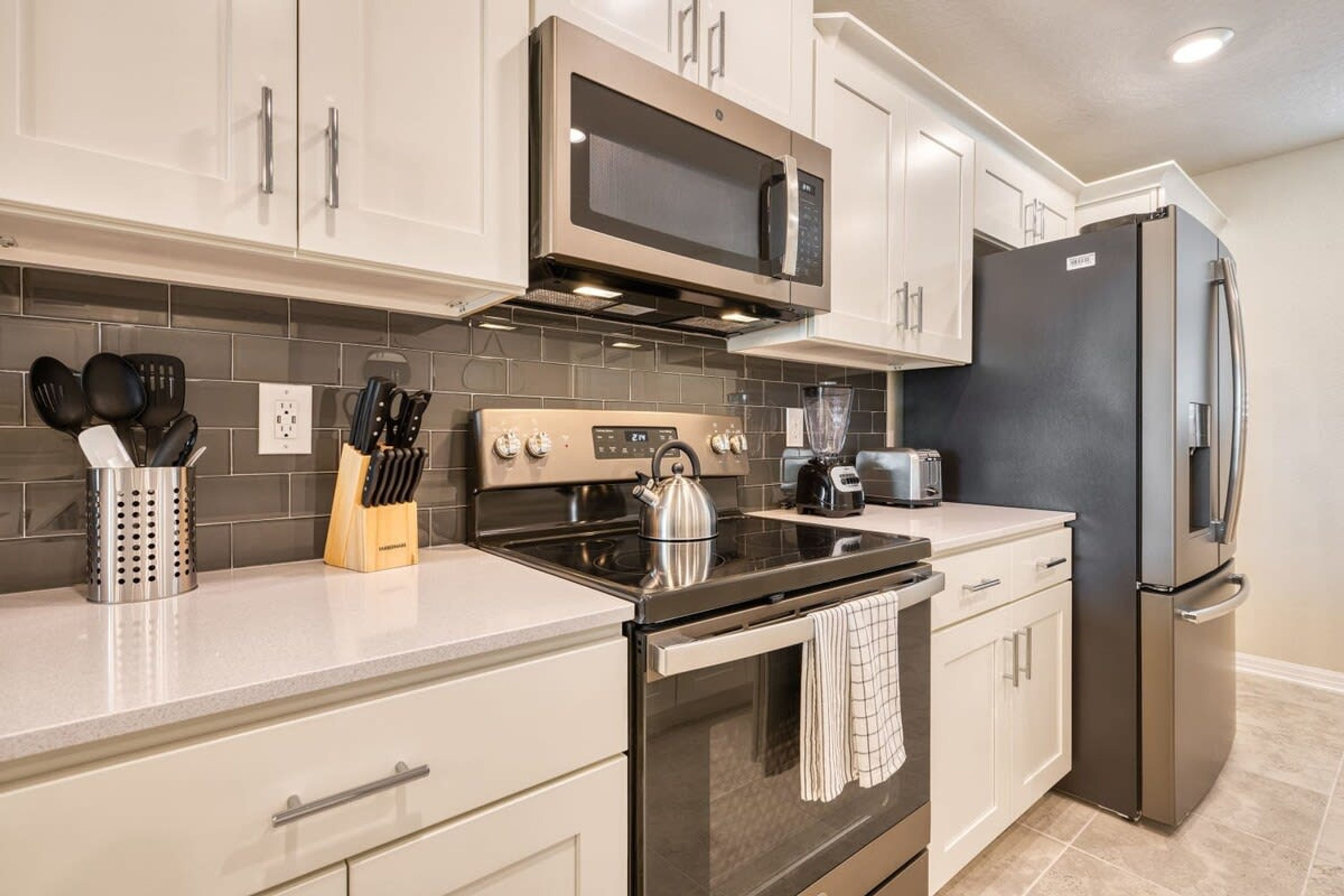 A modern kitchen with stainless steel appliances, white cabinetry, and a tiled backsplash.
