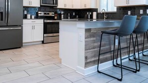 A modern kitchen with white cabinets, stainless steel appliances, and a central island with bar stools. - Modern Marvel-spacious Themed Fun-filled Family Getaway (Kissimmee)