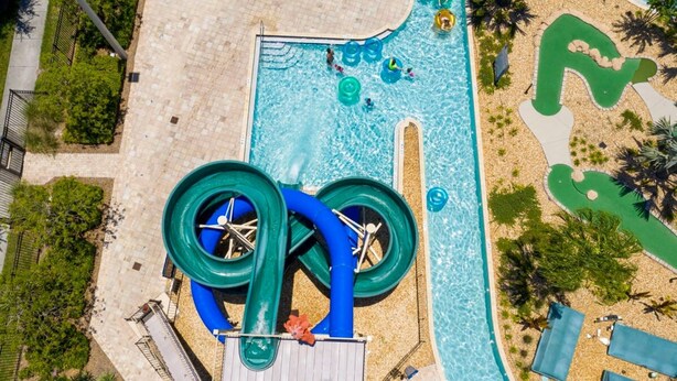 An aerial view of a water park with a large water slide, a pool, and surrounding greenery. - Modern Marvel-spacious Themed Fun-filled Family Getaway (Kissimmee)