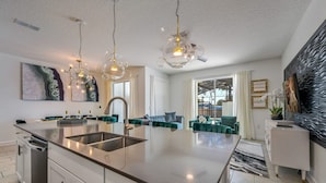Une cuisine moderne dotée d’un îlot central, d’appareils électroménagers en acier inoxydable et de luminaires suspendus.