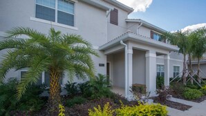 A modern two-story house with a well-maintained garden featuring palm trees and yellow flowering plants. - Prime Locale - Vacation Paradise (Kissimmee)