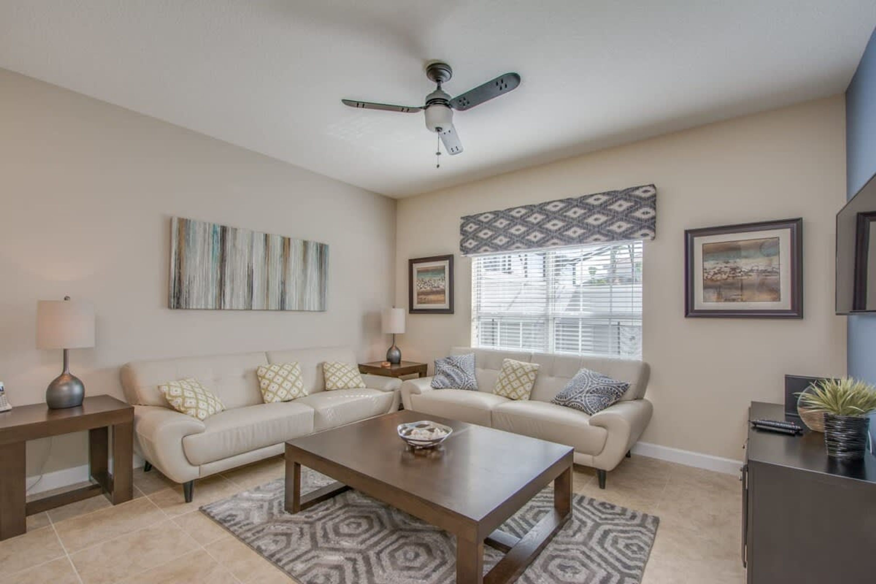 A living room with a sofa set, a coffee table, a ceiling fan, and a window with blinds.